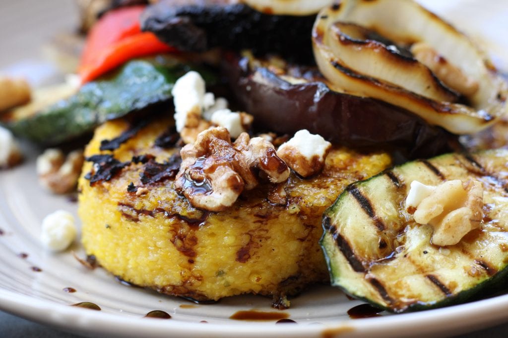 Rustic Italian Grilled Polenta & Vegetables recipe is a healthy & savory dish great for sharing. Polenta has flavors of rosemary and parmesan and is surrounded by grilled veggies and a balsamic reduction. Portable, tasty and vegetarian.