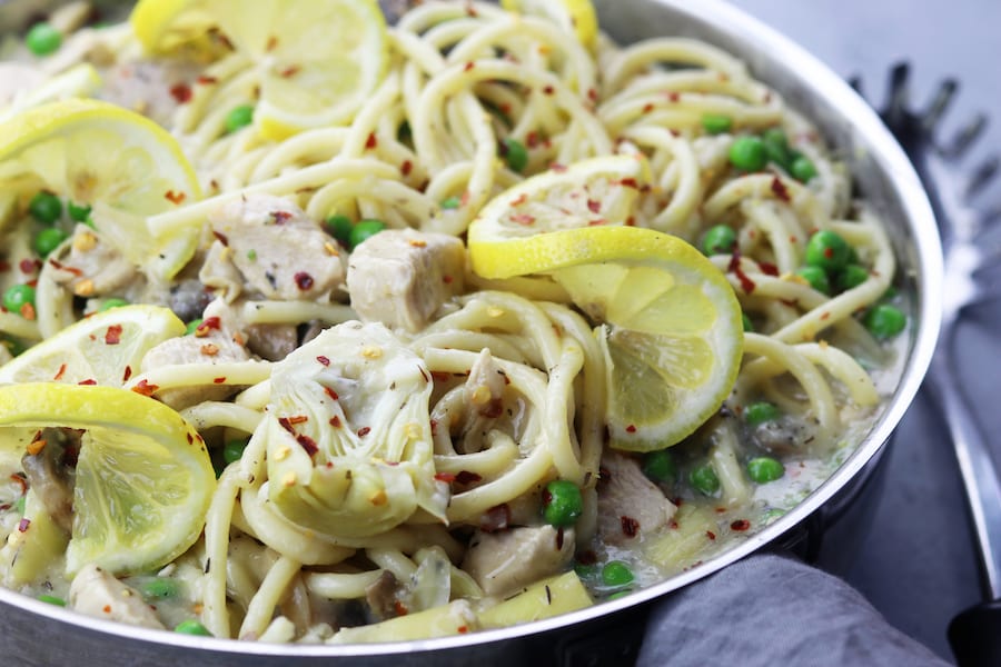 Skinny Lemon Chicken Pasta recipe is delicious enough for company and yet easy enough for a weeknight lighter meal. Tender chicken, artichoke hearts and peas are covered in a lemony garlic sauce. Serve with your favorite pasta, it is a favorite healthy decadent feast!