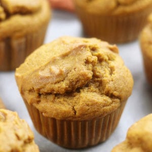 Up close photo of Pumpkin Spice Muffins sitting on a countertop along side a cinnamon stick.