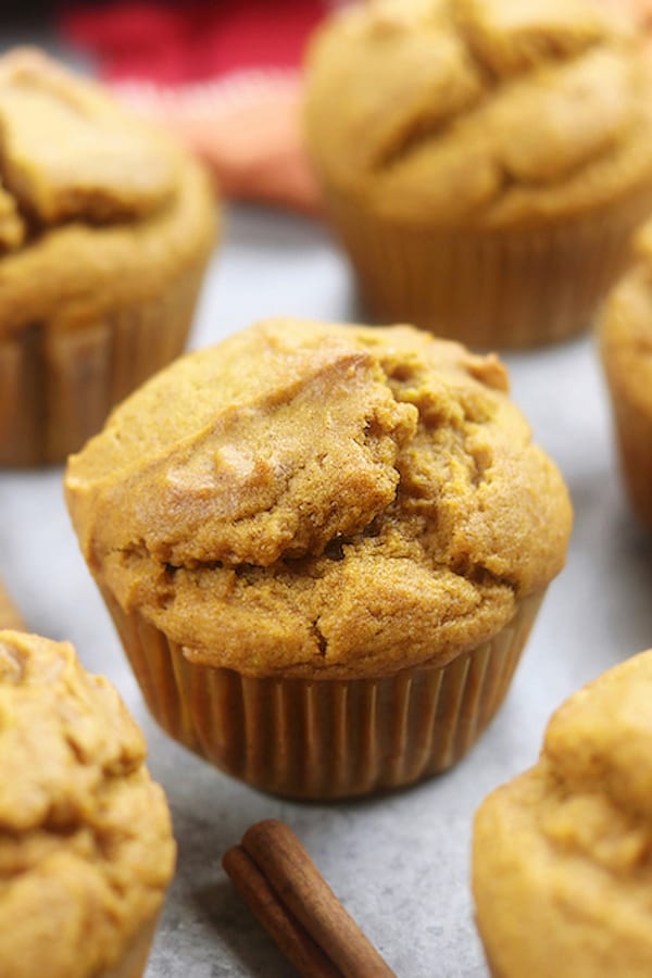 Up close photo of Pumpkin Spice Muffins sitting on a countertop along side a cinnamon stick.