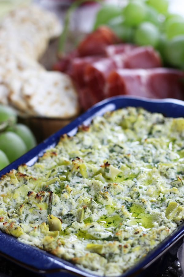 Best Artichoke Dip on a table with grapes, prosciutto and crackers.