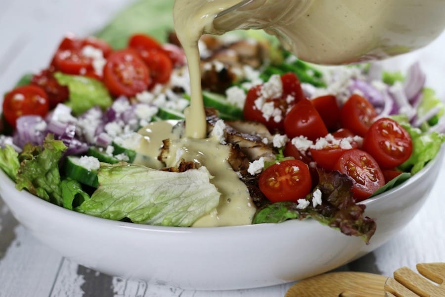 Poring of Tahini Lemon Summer Salad Dressing over a salad.