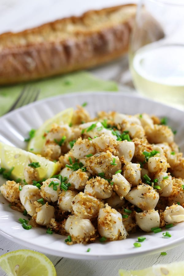 Broiled Scallops on a white plate with lemon slices and Panko crust.