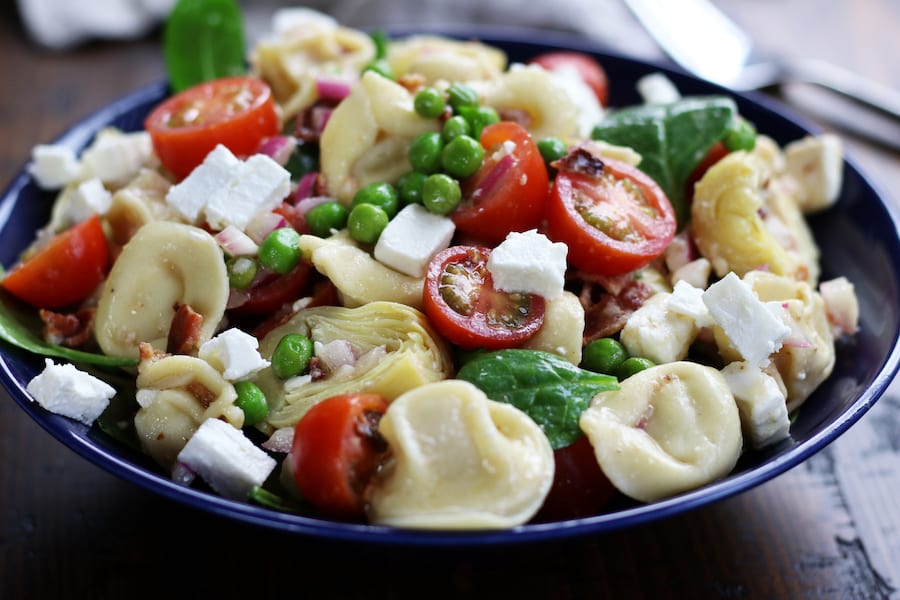 Tortellini Pasta Salad in a bowl with tomatoes, peas, bacon, feta and spinach.