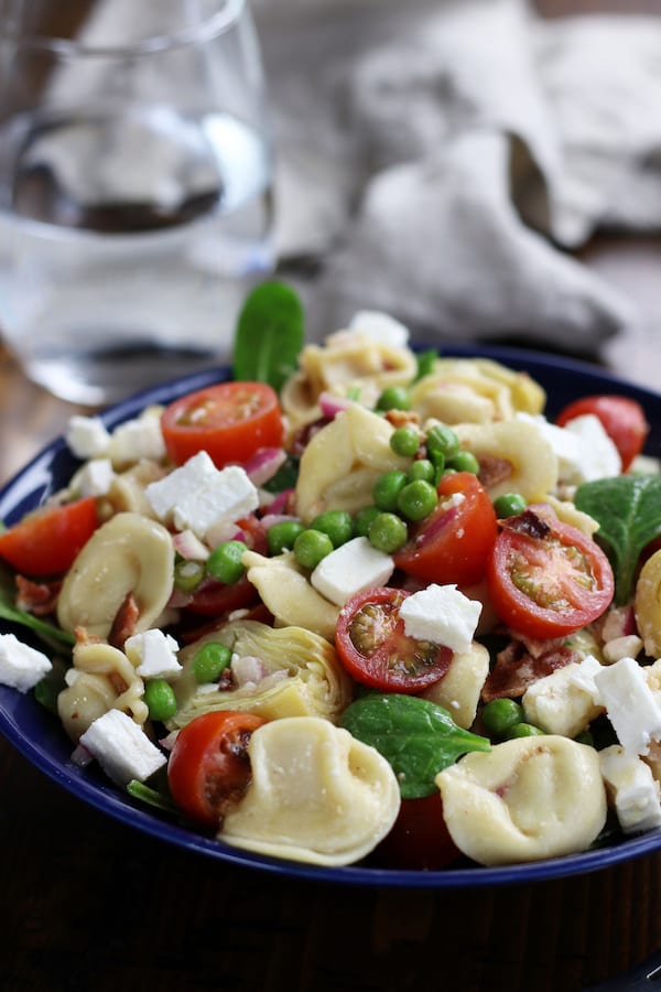 Tortellini Salad in a blue bowl with a glass water and a napkin.