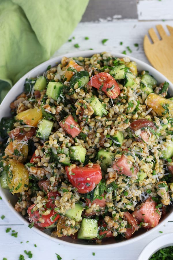 Overhead shot of Hulled Barley Salad in a white bowl on a white wooden surface.