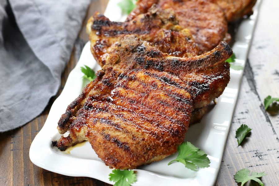 A white platter full of Baked Pork Chops sitting on a brown table.
