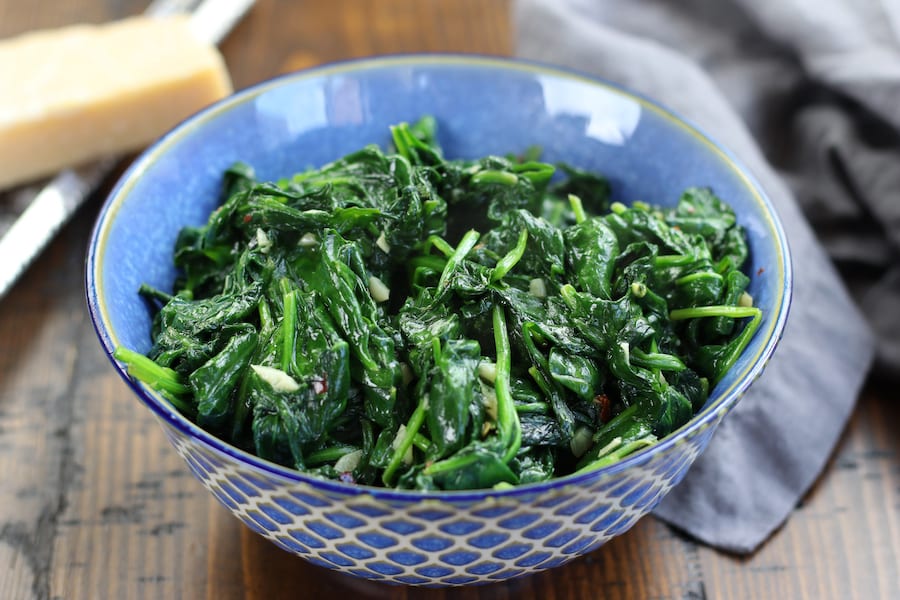 Italian Spinach recipe with minced garlic on a brown table.