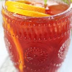 A glass of Passionfruit Drink with an orange curl and mint leaves.