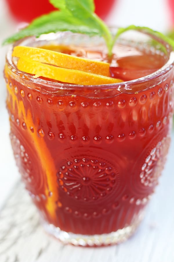 A glass of Passionfruit Drink with an orange curl and mint leaves.