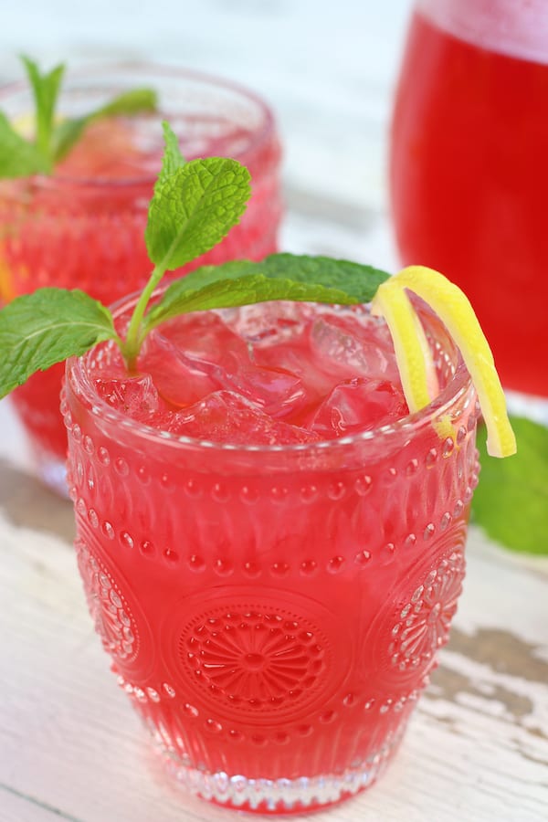 Two glasses and a pitcher of Pink Lemonade Recipe on a white table.