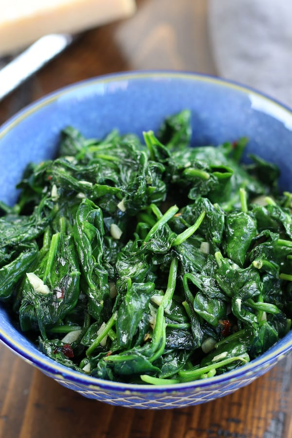 Wilted Spinach in a blue bowl with garlic and red chili pepper flakes.
