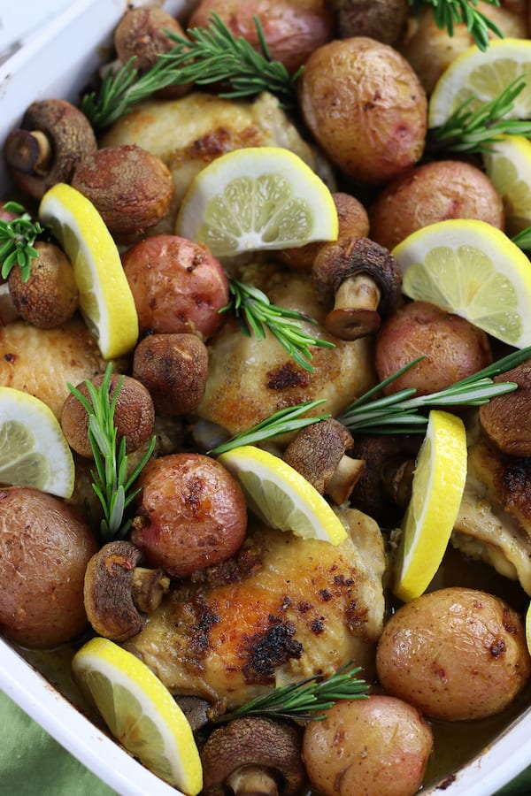 Chicken and Potatoes in a white roasting pan loaded with mushrooms, lemon wedges and rosemary.