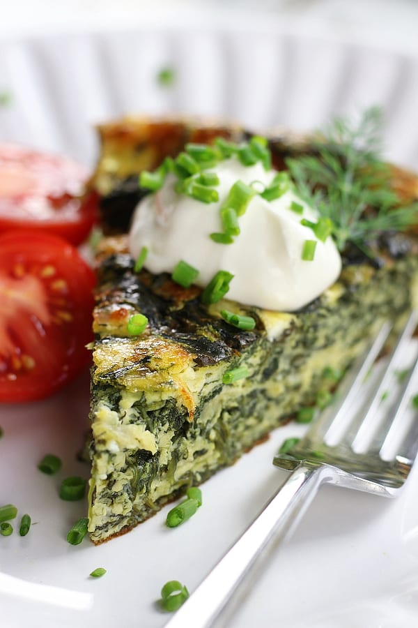 Piece of Crustless Spinach Quiche garnished with chives and sour cream.