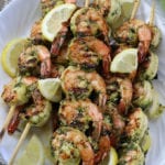 Marinated Grilled Shrimp Kabobs on a white plate with lemon wedges.