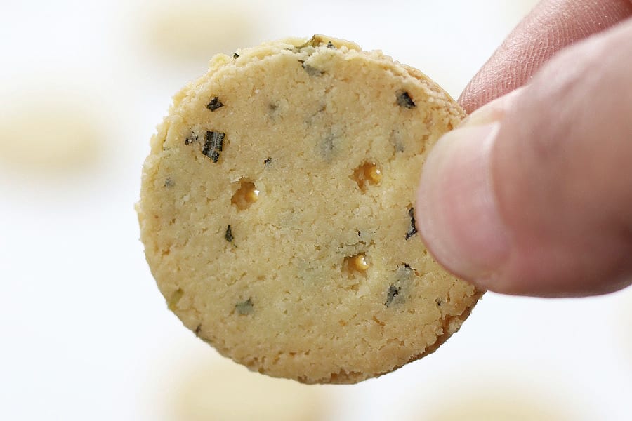 Up close shot of two fingers holding a Rosemary Parmesan Almond Crackers.