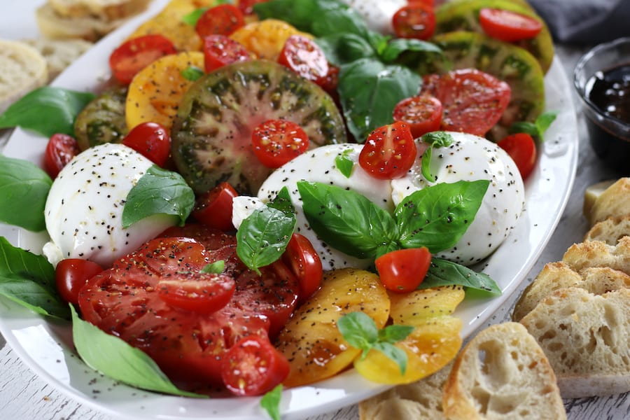 Caprese Salad Recipe served on a platter with fresh cut baguette bread.