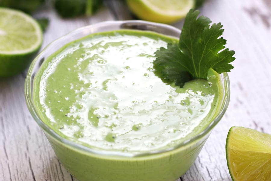 Overhead photo of Cilantro Cream Sauce on a white table with limes.