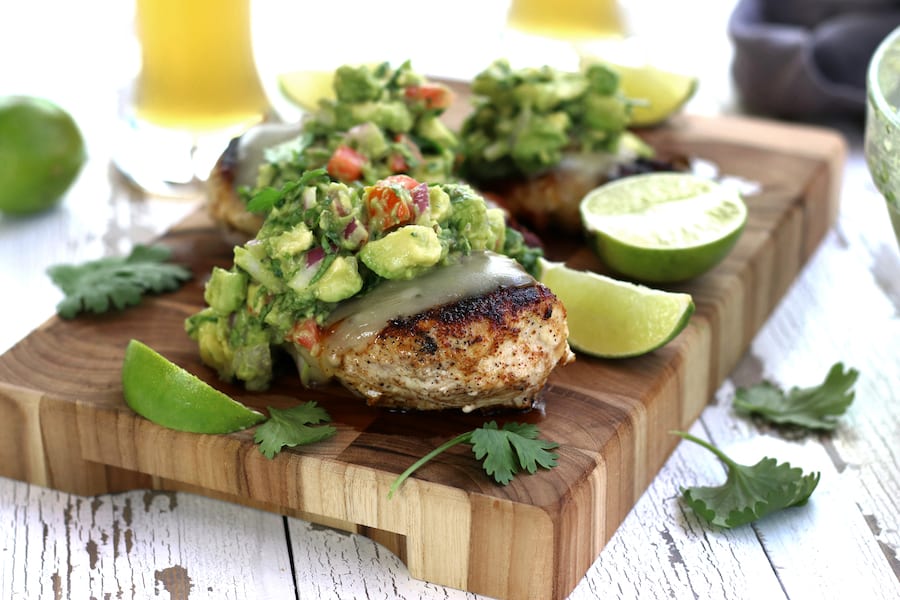 Guacamole Chicken breast resting on a cutting board with lime slices and topped with guac.