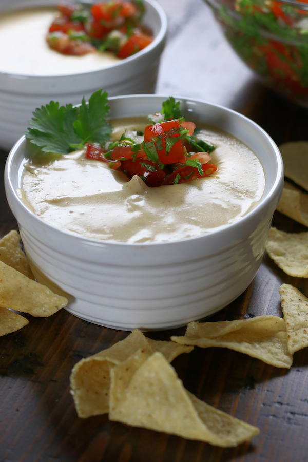 Nacho Cheese Recipe displayed in two small bowls on a brown table surrounded by chips.