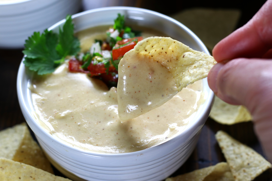 A small white bowl of Nacho Cheese Sauce with salsa and cilantro.