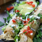 Chicken Flautas on a plate garnished with tomatoes, cilantro and avocado.