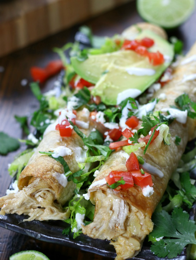 Chicken Flautas on a plate garnished with tomatoes, cilantro and avocado.