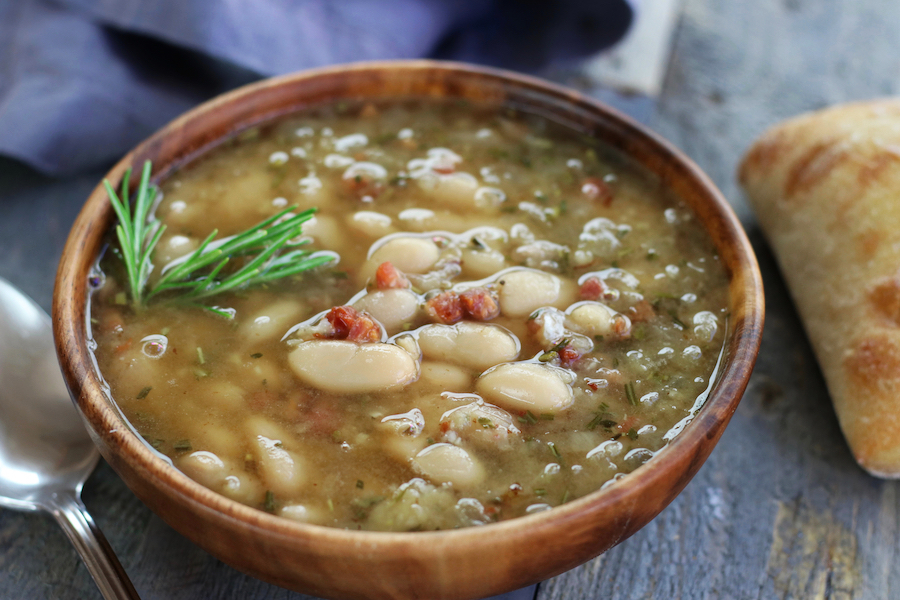 Mediterranean White Bean Soup in a brown bowl sitting on a grey table.