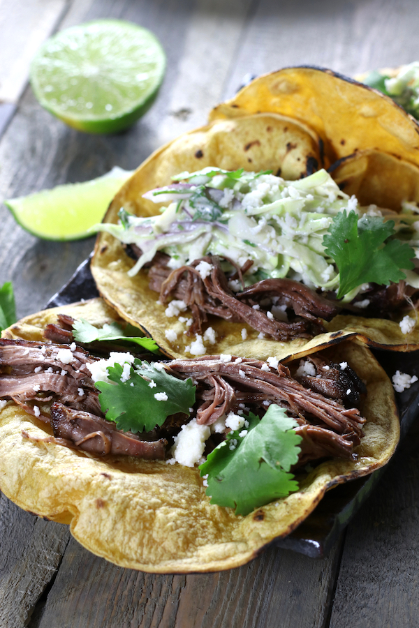 Mexican Shredded Beef Tacos sitting on a wooden table with lime wedges.