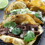 Three Shredded Beef Tacos with Cilantro Lime Coleslaw sitting on a grey plate.