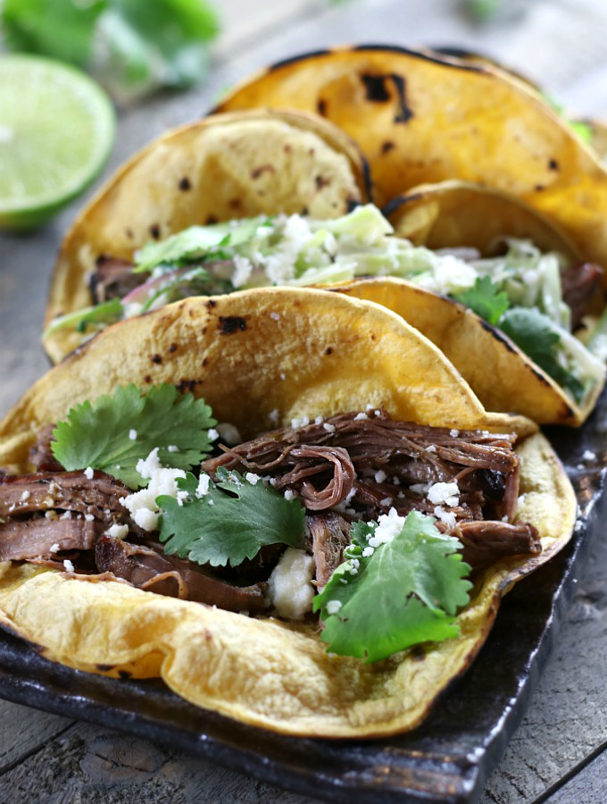 Three Shredded Beef Tacos with Cilantro Lime Coleslaw sitting on a grey plate.