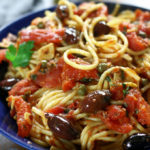 A serving of Spaghetti alla Puttanesca in a blue pasta bowl.