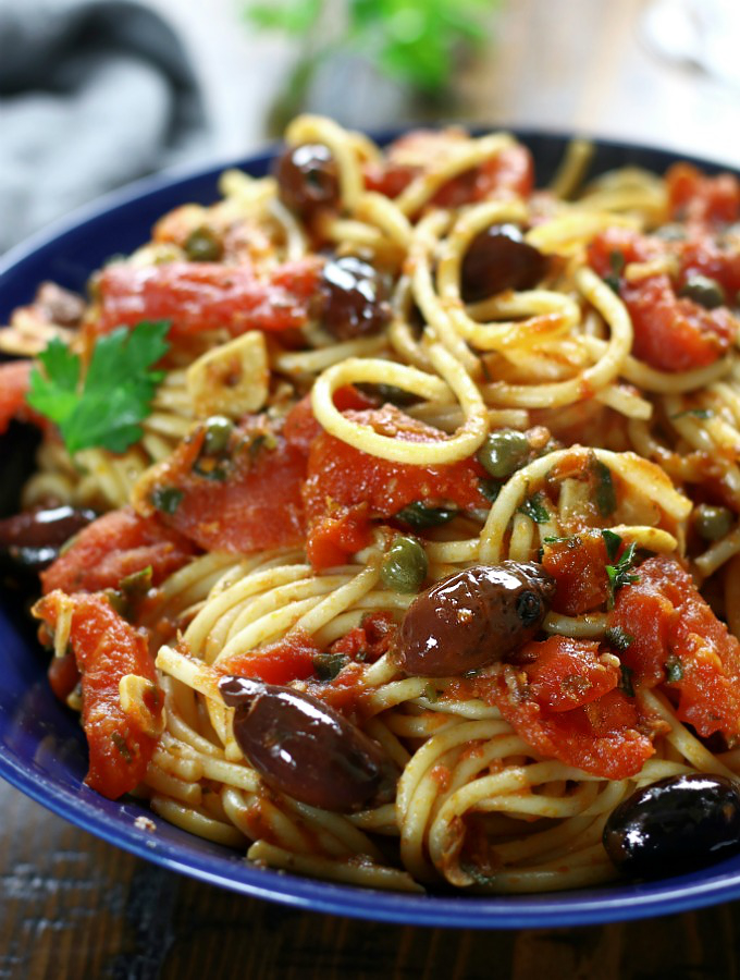 A serving of Spaghetti alla Puttanesca in a blue pasta bowl.