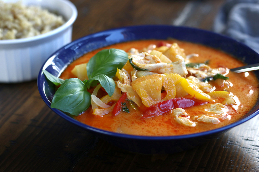 A bowl of Chicken and Pineapple Curry sitting on a table next to a small white bowl of cook rice.