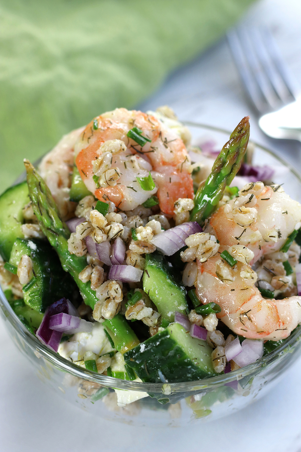 Farro Salad in a glass bowl with diced red onion, asparagus, shrimp and cucumbers.