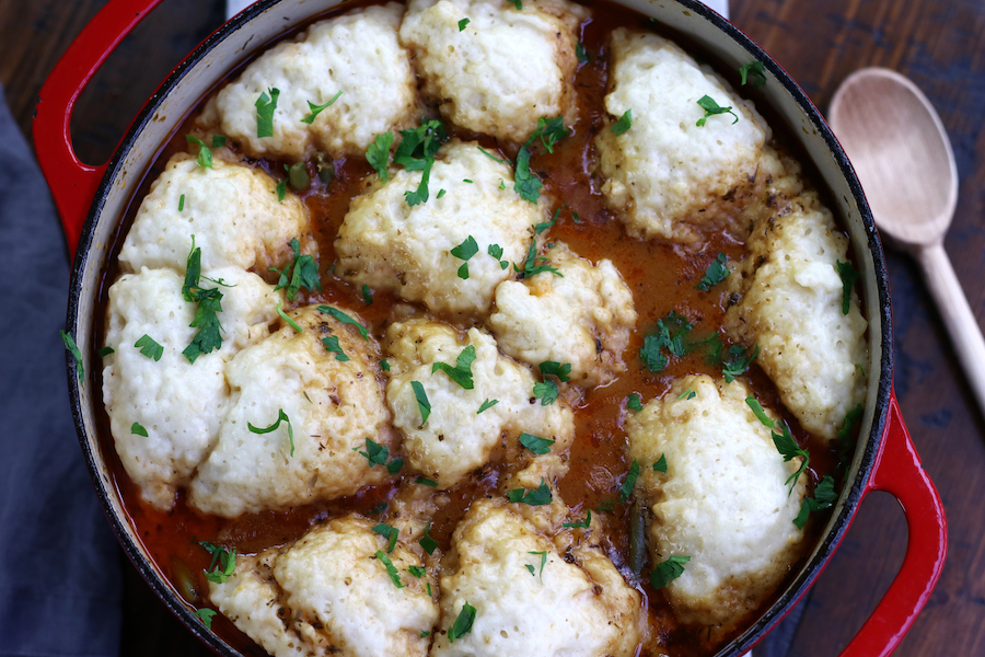 Overhead photo of Beef Stew and Dumplings Recipe in a red pot sitting on a brown table.