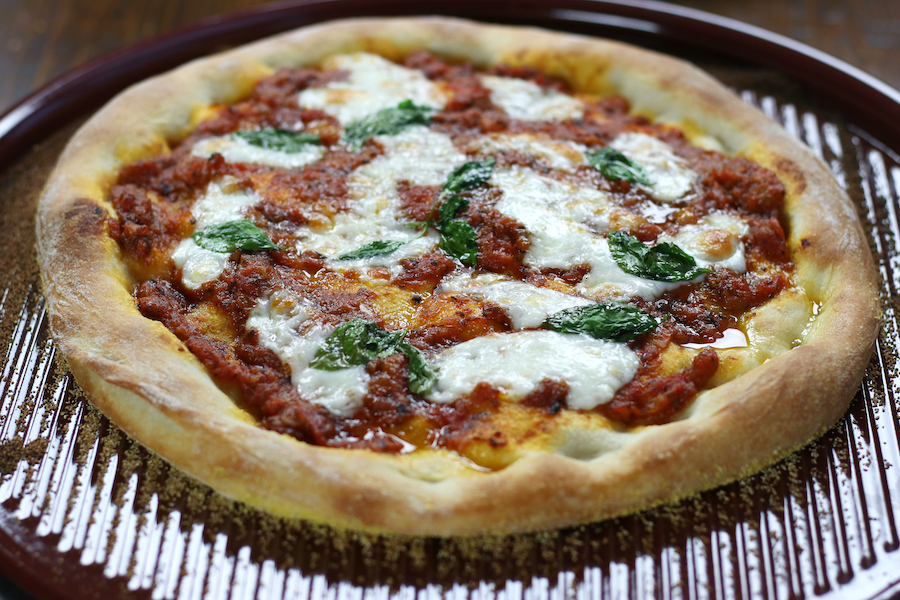 Pizza Napolena sitting on a red pizza stone.