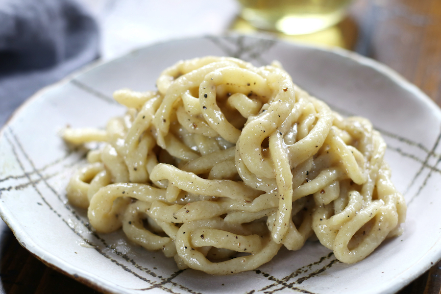 Up close photo of Cheese and Pepper Pasta sitting on a brown table with a glass of wine.