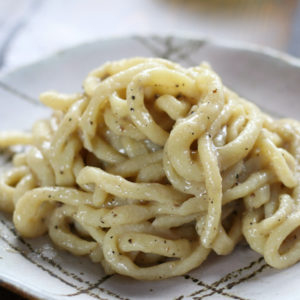 A serving of Pasta Cacio e Pepe on a grey lined plate sitting on a brown table.