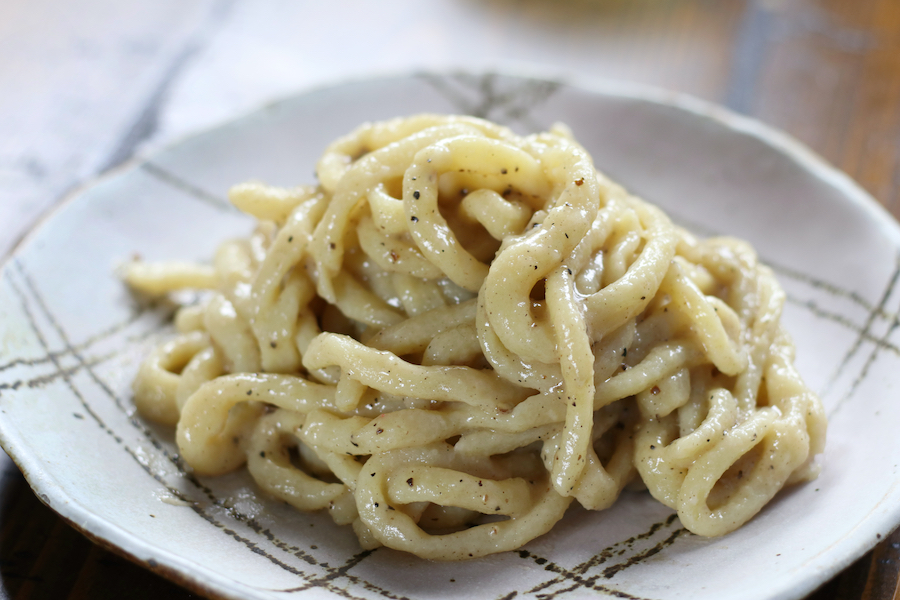 A serving of Pasta Cacio e Pepe on a grey lined plate sitting on a brown table.