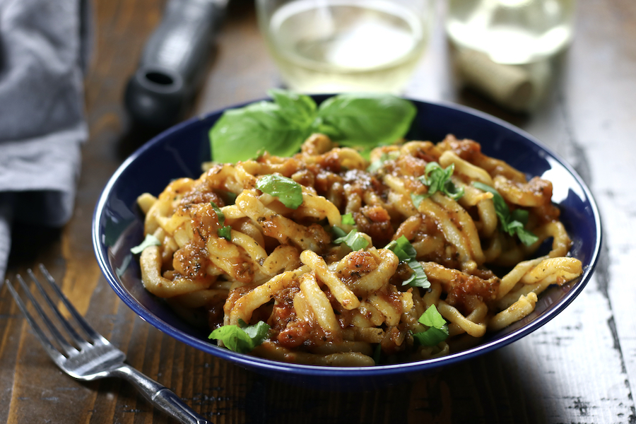 Pici Aglione in a blue bowl sitting on a brown table.