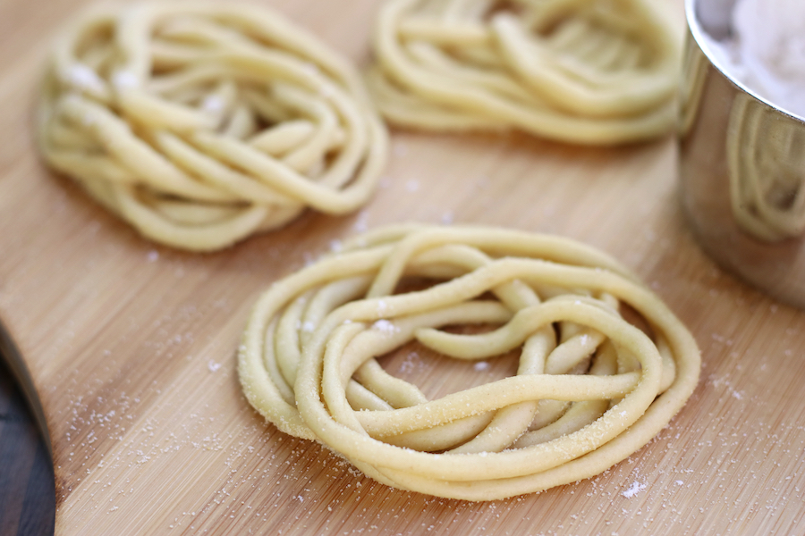 Hand rolled Pici Toscani sitting on a natural wood colored board.