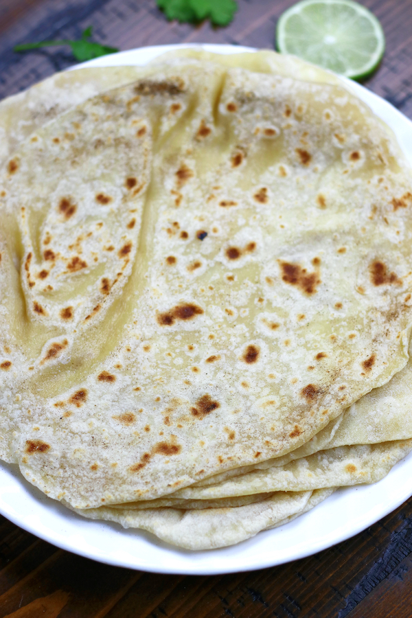 Fresh tortillas on a white plate with a slice of lime.