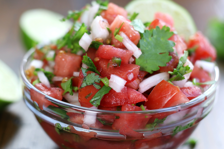 A big bowl of Pico de Gallo Salsa sitting on a brown table.