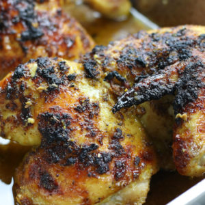 Two roasted chicken halves in a roasting pan from Citrus Chicken recipe.