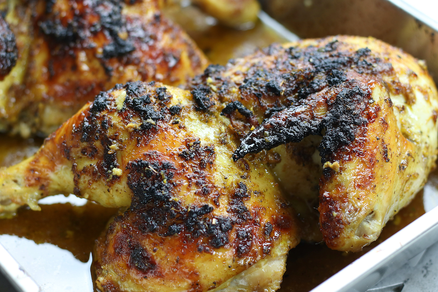 Two roasted chicken halves in a roasting pan from Citrus Chicken recipe.