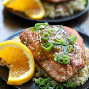 Two plates of Orange Glazed Salmon ditto on a wooden surface.