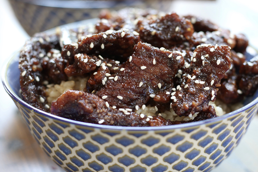 Crispy Beef sitting on a bed of brown rice that is garnished with sesame seeds.