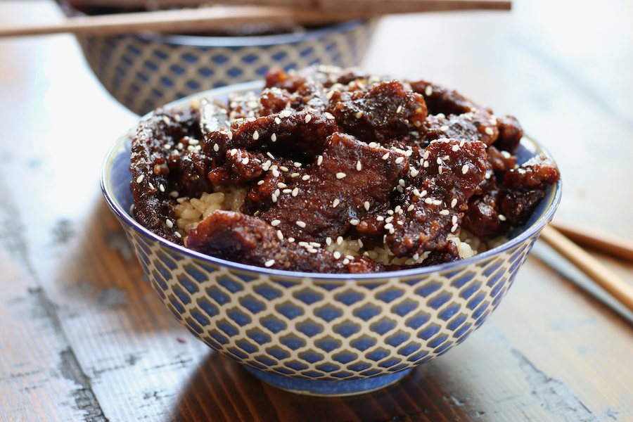 Two blue patterned bowls of Crispy Ginger and Sesame Beef sitting on a brown table.