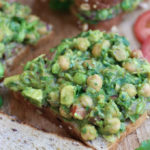 An open faced Guacamole Chickpea Salad Sandwich on a wooden cutting board.